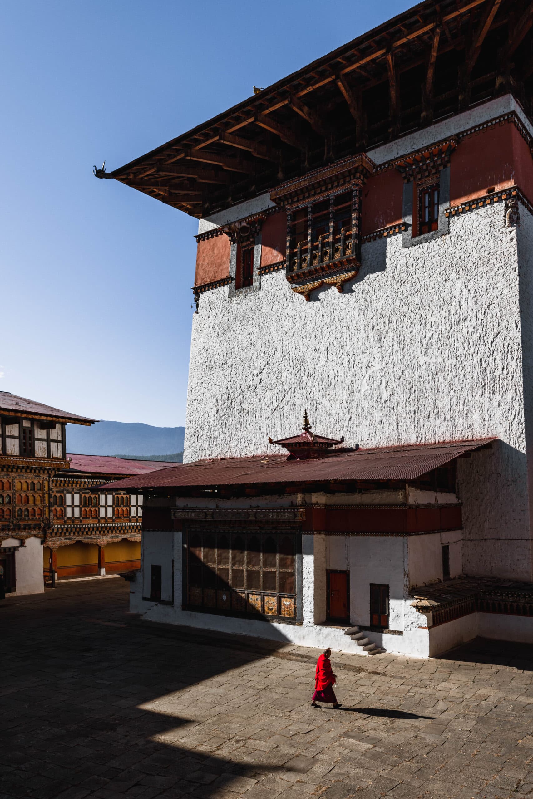 Monk walking through a sunlit dzong courtyard in Paro, Bhutan after the Tsechu festival